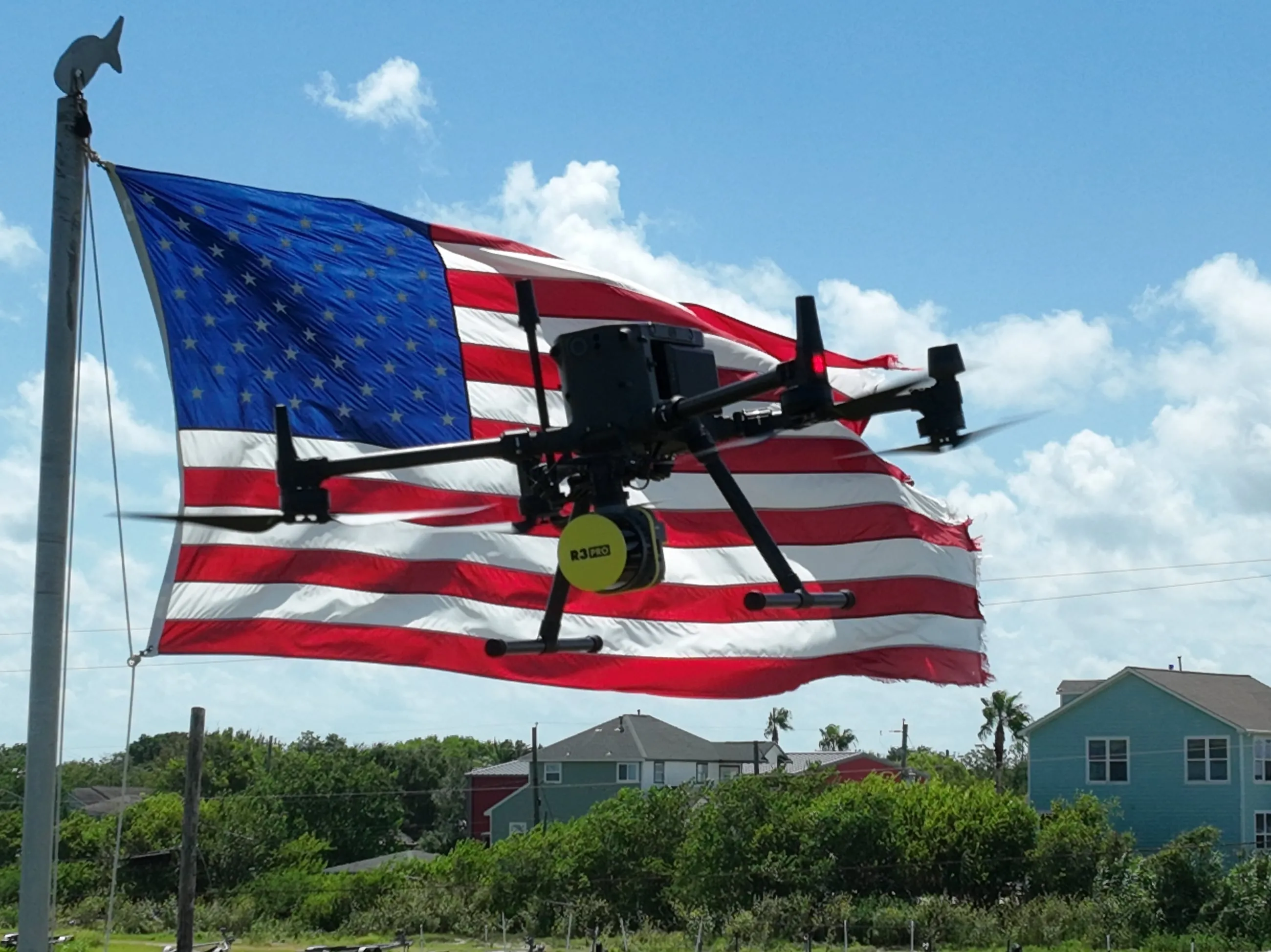 Axis survey aircraft holding station in front of a full American flag, LiDAR payload mounted below.