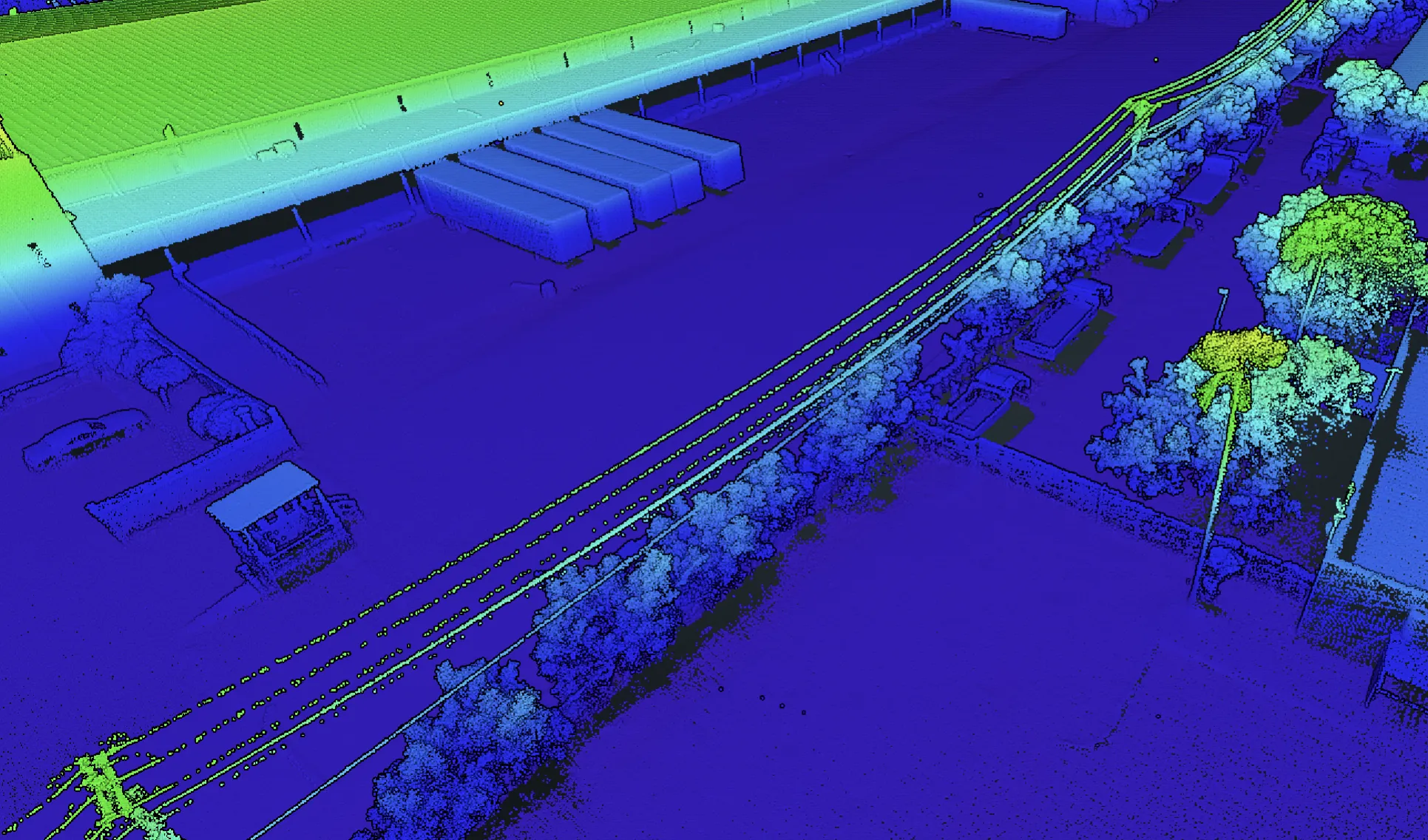 Elevation-colorized LiDAR point cloud of the full Loera Brokerage warehouse site: the warehouse roof reads as a green plane over the blue ground field, with docked trailers and rail spur alongside.